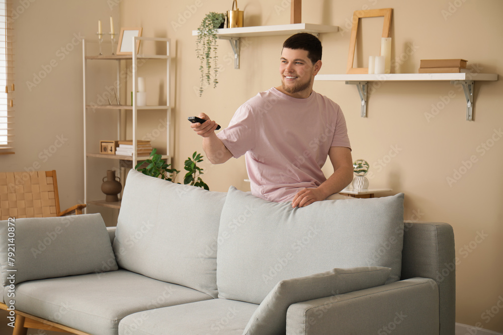 Young man with remote control watching TV in living room Young man with remote control watching TV in living room