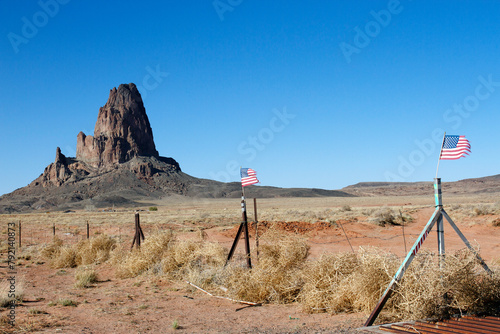 An impressive rock formation and two American flags along a rural road in Arizona