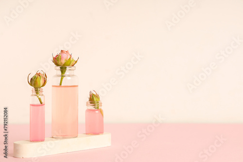 Composition with bottles of cosmetic oil, plaster stand and roses on pink background