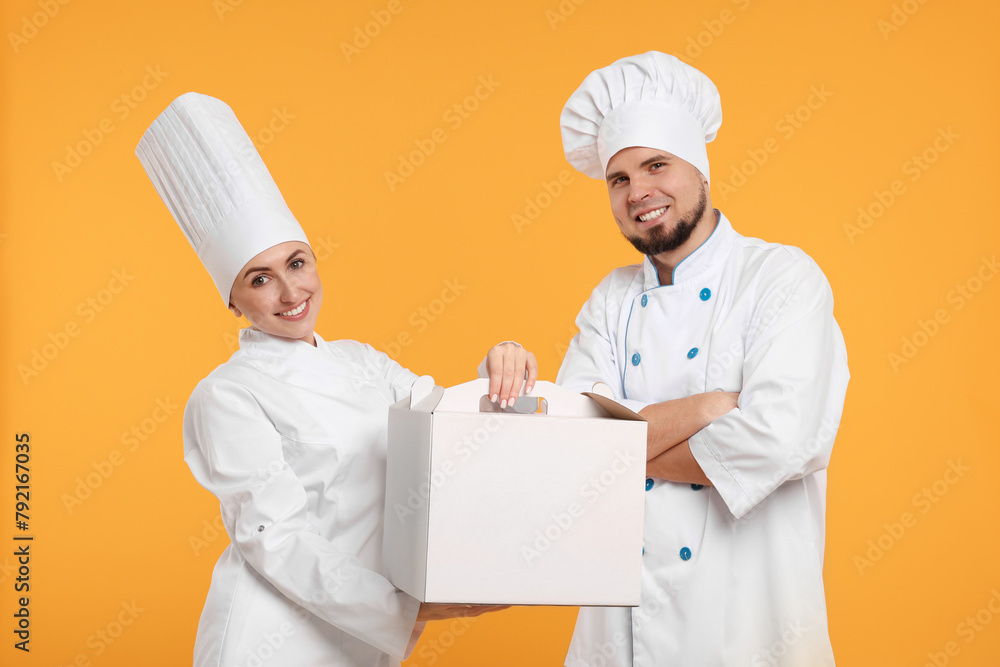 Happy professional confectioners in uniforms holding cake box on yellow background
