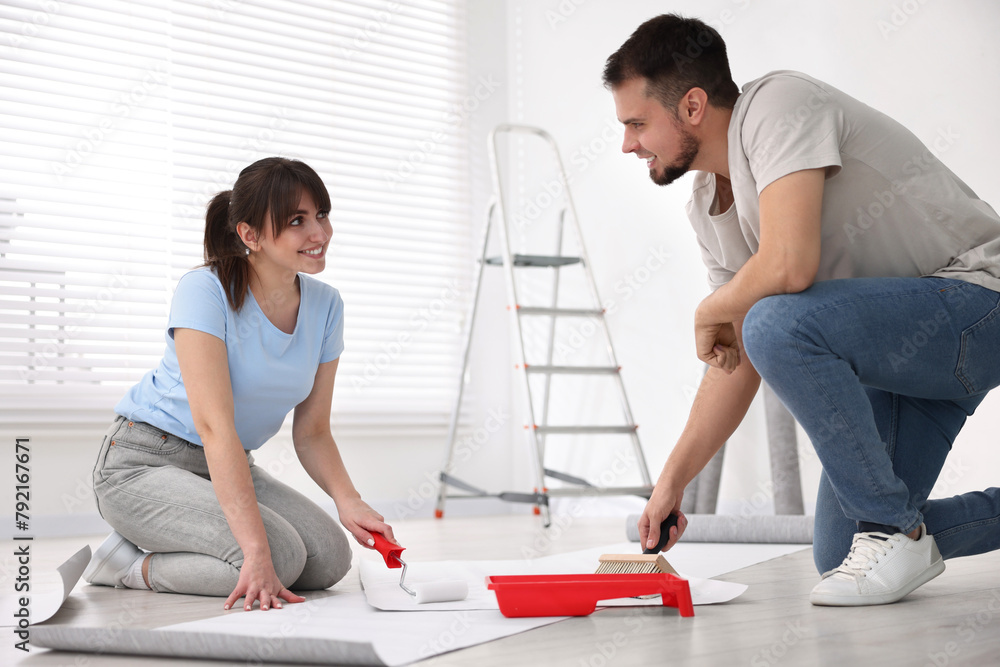 Obraz premium Couple applying glue onto wallpaper sheet in room
