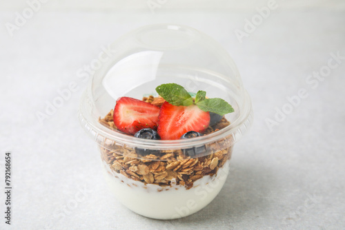 Tasty granola with berries and yogurt in plastic cup on light table, closeup