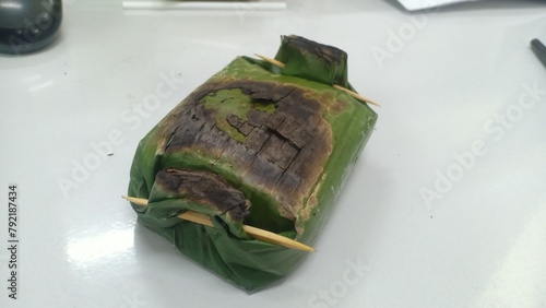 a packet of grilled rice wrapped in banana leaves, grilled over a charcoal fire filled with rice flavored with turmeric and other spices, anchovies and basil leaves, served warm.

