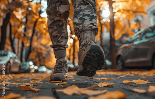 A person in camouflage pants is walking on a sidewalk with leaves on the ground