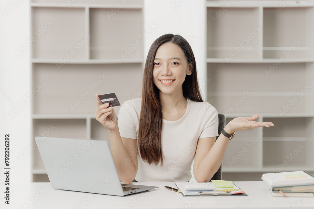 Smiling young woman holds credit card while sitting with laptop at home, shopping online, holding credit card, paying on Internet banking and e-commerce applications Smiling young woman holds credit card while sitting with laptop at home, shopping online, holding credit card, paying on Internet banking and e-commerce applications