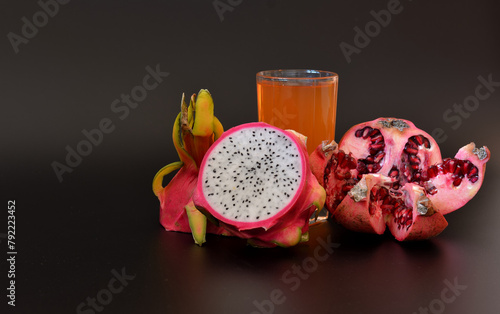 A glass of freshly squeezed fruit juice on a black background, next to pieces of ripe pitaya and a pomegranate fruit with seeds.
