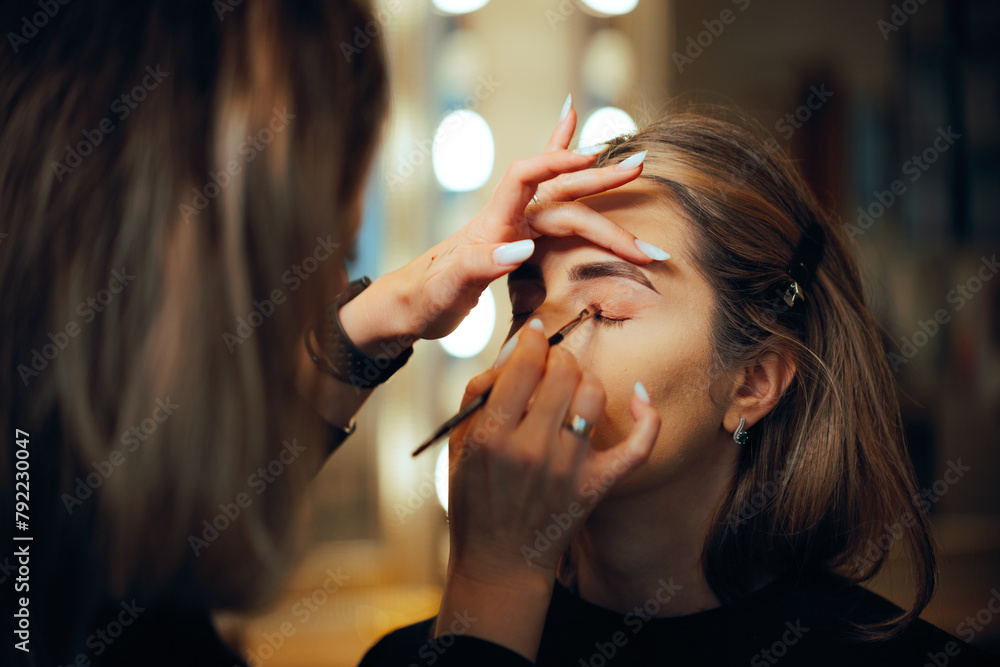 Fototapeta Professional Make-up Artist Applying Eyeshadow with a Brush. Woman having her looks changed through professional makeup 

