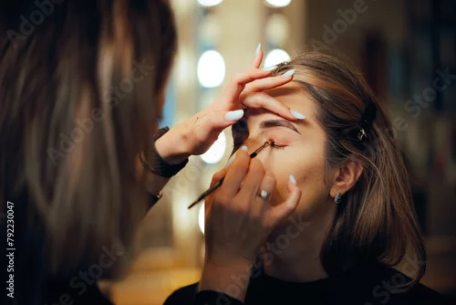 Obraz Professional Make-up Artist Applying Eyeshadow with a Brush. Woman having her looks changed through professional makeup 
