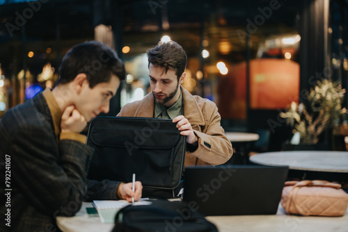 Two focused male business professionals engage in a project discussion at a cafe, strategizing for company success.