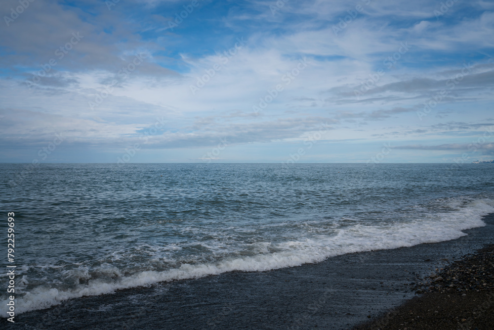 An incoming wave on the Black Sea and a pebble beach on the Sochi coast on a sunny summer day with clouds, Sochi, Krasnodar Territory, Russia An incoming wave on the Black Sea and a pebble beach on the Sochi coast on a sunny summer day with clouds, Sochi, Krasnodar Territory, Russia
