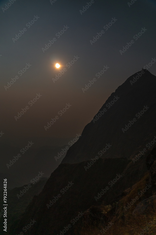 A mountain with a large moon in the sky A mountain with a large moon in the sky