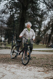 An active senior woman with a bright smile stands with her bicycle in a tranquil park, embodying a healthy lifestyle.