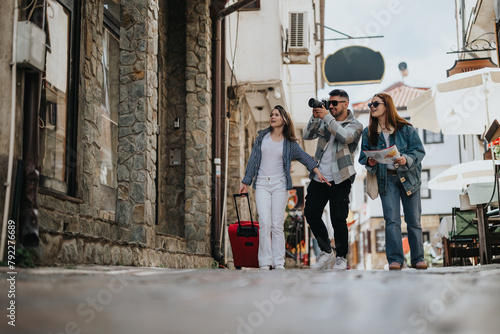 Three young tourists with a suitcase casually exploring a picturesque European city street, capturing memories and consulting a map on a sunny day. © qunica.com