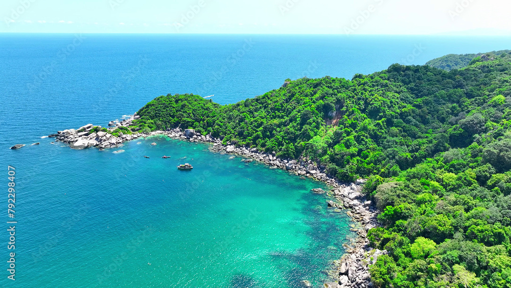 Where lush forests meet the shore, peculiar rock formations adorn the coastline, bathed in the serene blue of the clear, turquoise waters. Flying from drone. Tao island, Thailand.
