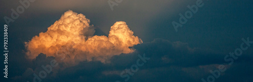 Cloud in the sky at sunset. The cloud is illuminated by the rays of the sun on the dark sky in the evening. A light cloud among thunderclouds in the sky.