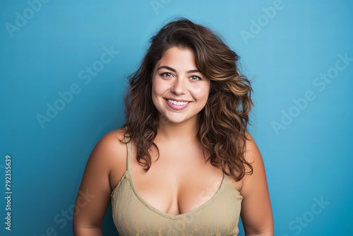smiling curvy woman looking at camera, standing against blue background, chubby, overweight