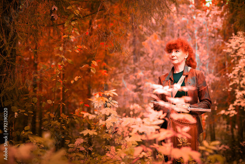 Mature model portraying a royal huntress with red curve hair is hunting with a crossbow in the in vibrant autumn forest in a thematic photo shoot