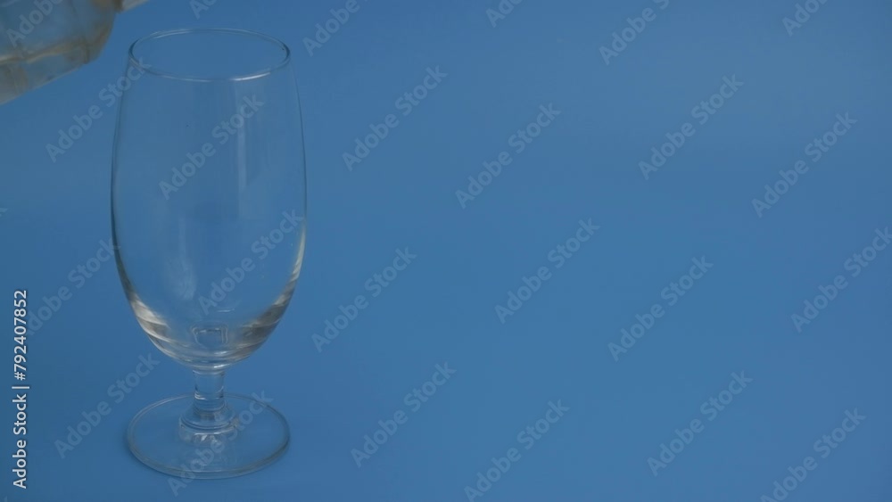 Pouring water from bottle into glass on blue background. Copy space for text. Pouring water from bottle into glass on blue background. Copy space for text.