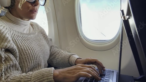 One adult woman travel on airplane on board using laptop computer sitting on the seat near thw window. Traveler on aircraft. Flight business online with computer. Modern traveler working and fly photo