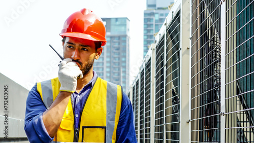 Asian male technical foreman inspects maintenance work holding a tablet and commands with talking on radio call with colleague with to look at air conditioning system assembled on top of a building