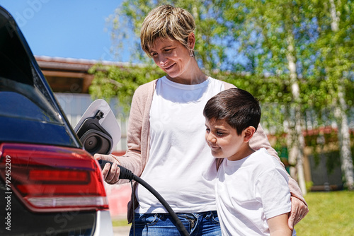 Young boy learns to charge EV from his mother on a sunny day.