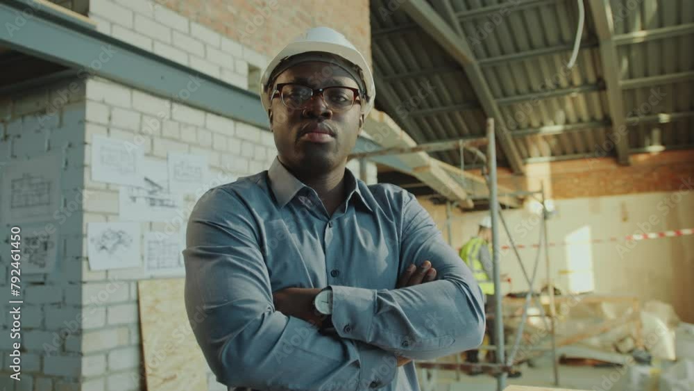 Confident Black architect wearing hardhat and formalwear posing at camera with arms folded during workday on construction site. Zoom shot, video portrait Confident Black architect wearing hardhat and formalwear posing at camera with arms folded during workday on construction site. Zoom shot, video portrait