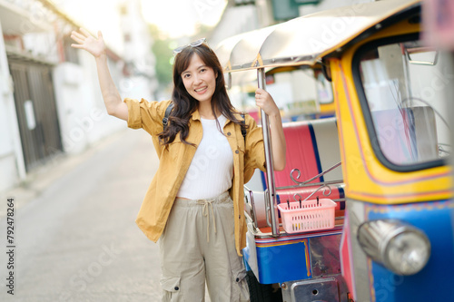 Young Asian woman backpack traveler standing a side of Tuk Tuk taxi on summer vacations at Bangkok, Thailand. Journey trip lifestyle, Asia summer tourism concept.