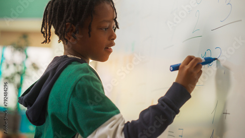 Portrait of a Handsome African Boy Finding a Solution to a Mathematical Task on a Whiteboard in Class in Elementary School. Young Pupil is Focused on Numbers, Writing Down a Correct Answer