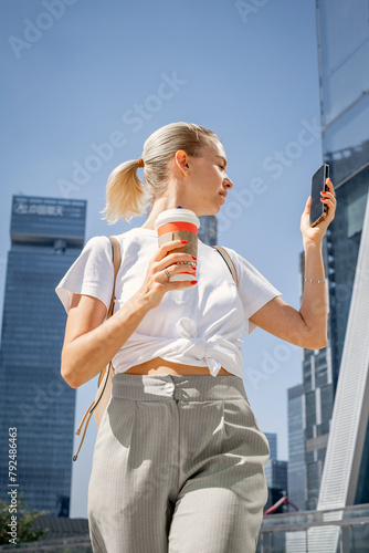 Portrait of a young woman with a phone and a cup of coffee in the business center of the city