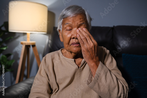 senior woman with eye fatigue while sitting on sofa in the living room at night