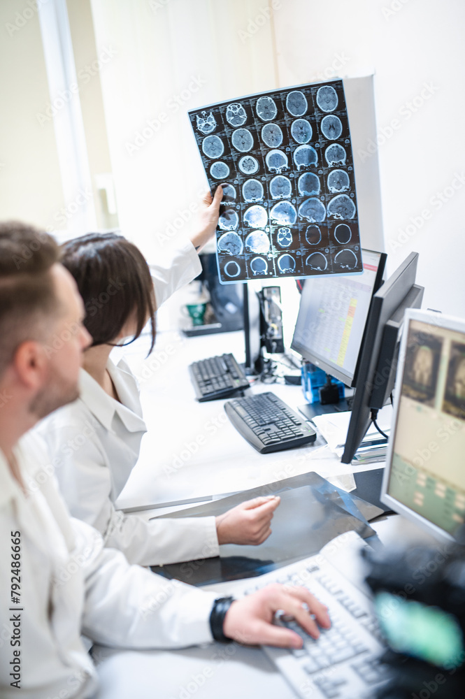 Doctors in the MRI room sit at a computer monitoring the progress of the procedure. A council of doctors examines an MRI image. Blurred image Doctors in the MRI room sit at a computer monitoring the progress of the procedure. A council of doctors examines an MRI image. Blurred image