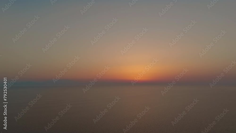Drone records the sun setting over the sea with a clear sky and minimal cloud cover Drone records the sun setting over the sea with a clear sky and minimal cloud cover