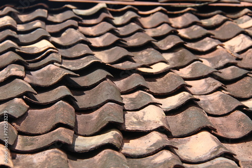 Close-up of a red-brown tile roof of a house with a blurred blue sky in the background on a sunny morning