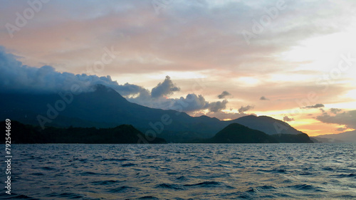 Sunset over a tropical island. View of the silhouette of a tropical island and clouds colored by the rays of the setting sun.