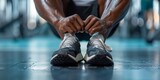 An unknown black athlete sits alone in gym stretching legs. Black man in shape preparing to workout in center. Exercise warmup before health and weight training
