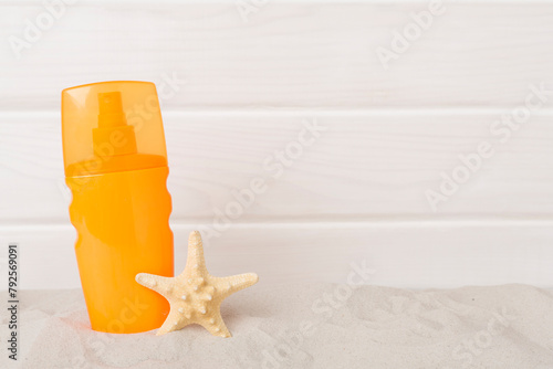 Sunscreen lotion with summer decor on sand against wooden background