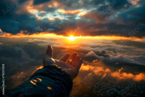 A hand is raised in the air, reaching towards the sun. The sky is filled with clouds, creating a moody atmosphere. Concept of hope and longing photo