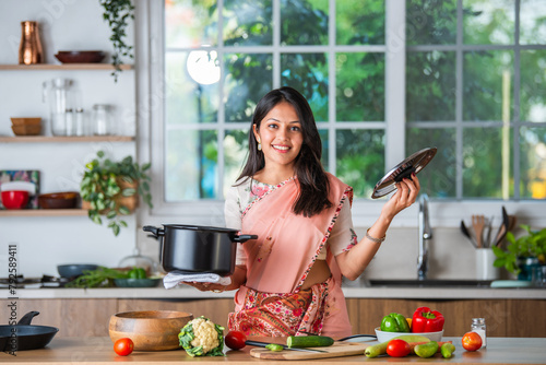 Hppy young asian indian woman in kitchen promoting utensils and ok sign © StockImageFactory