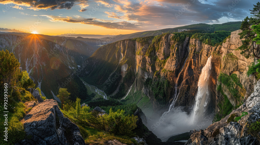Beautiful panoramic view of waterfall and mountains at sunset with golden sunlight shining on the mountains in summer