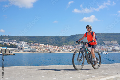 nice senior woman cycling with her electric mountain bike on the fishermens jetty of Sesimbra, Portugal photo