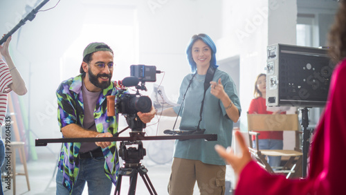 Young Caucasian Male And Female Filmmakers Collaborate On A Film Set, Adjusting Camera Equipment With Enthusiasm, Surrounded By Diverse Crew Members In A Bright, Modern Studio Environment. © Gorodenkoff