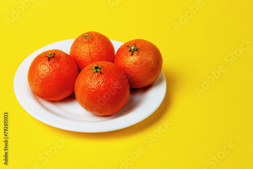 Delicious sweet mandarin fruits on a white plate with a yellow background and space for a copy