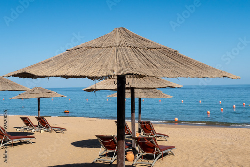 Sandy beach in Fujairah, United Arab Emirates, with thatch umbrellas and sunbeds, sea view and blue sky, no people.