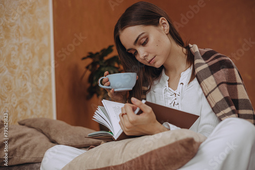 Focused woman with cup of tea reading book at home