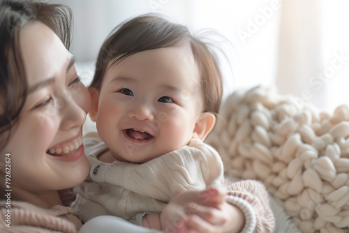 Loving mother hugs a little baby at home. Pretty woman holding cuddling newborn child in her arms, laughing with him. Happy family smiling together. Asian mom carrying kissing small infant on hands.