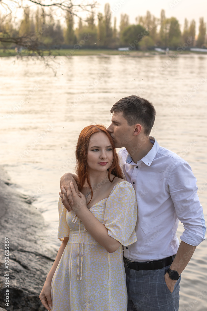 Young couple in love standing by the lake, the man kisses the woman on her hair. Young couple in love standing by the lake, the man kisses the woman on her hair.