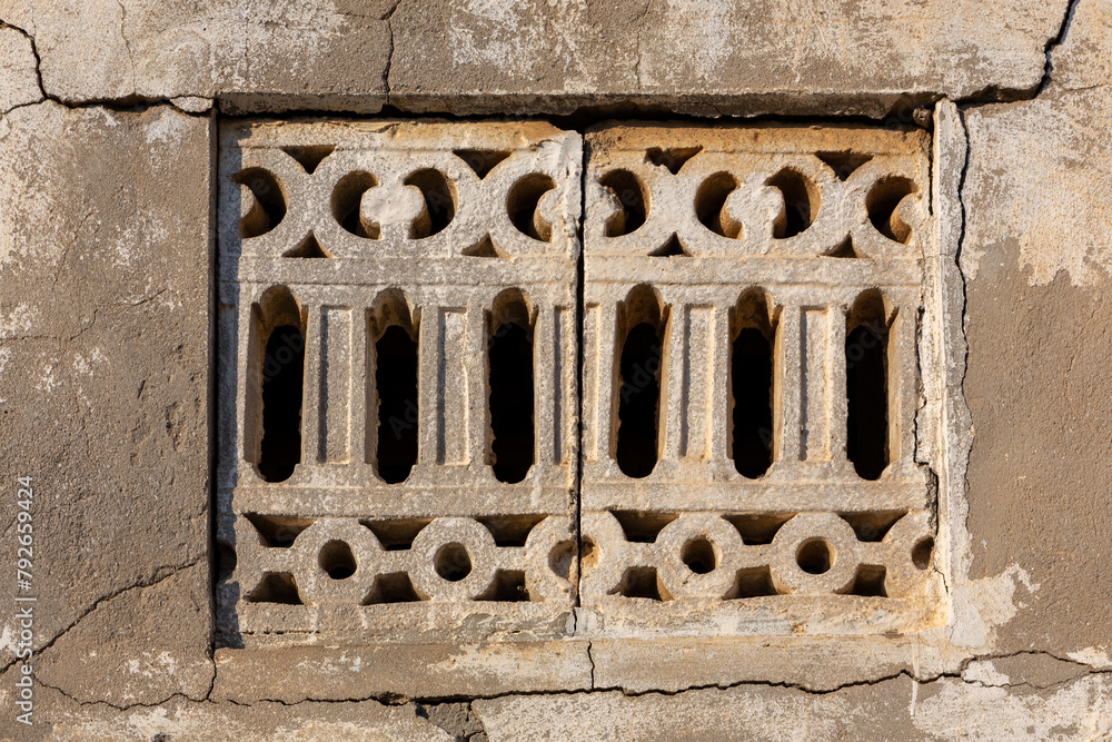 Arabic style old stone carved window with cracked stone wall around in Al Jazirah Al Hamra abandoned village in Ras Al Khaimah, United Arab Emirates. Arabic style old stone carved window with cracked stone wall around in Al Jazirah Al Hamra abandoned village in Ras Al Khaimah, United Arab Emirates.