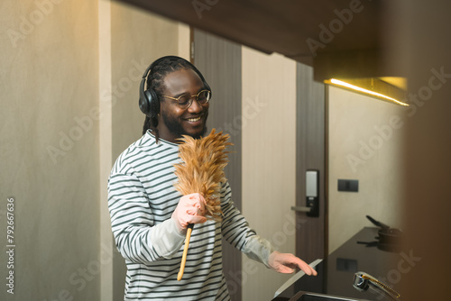 Carefree African man enjoying housework singing while cleaning kitchen
