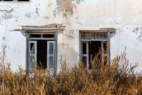 Neglected building facade with broken windows and blue window shutters in Al Jazirah Al Hamra haunted town in Ras Al Khaimah, United Arab Emirates. photo