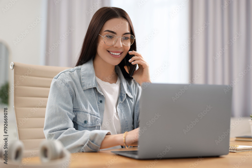 Young woman talking on smartphone during webinar at table in room Young woman talking on smartphone during webinar at table in room